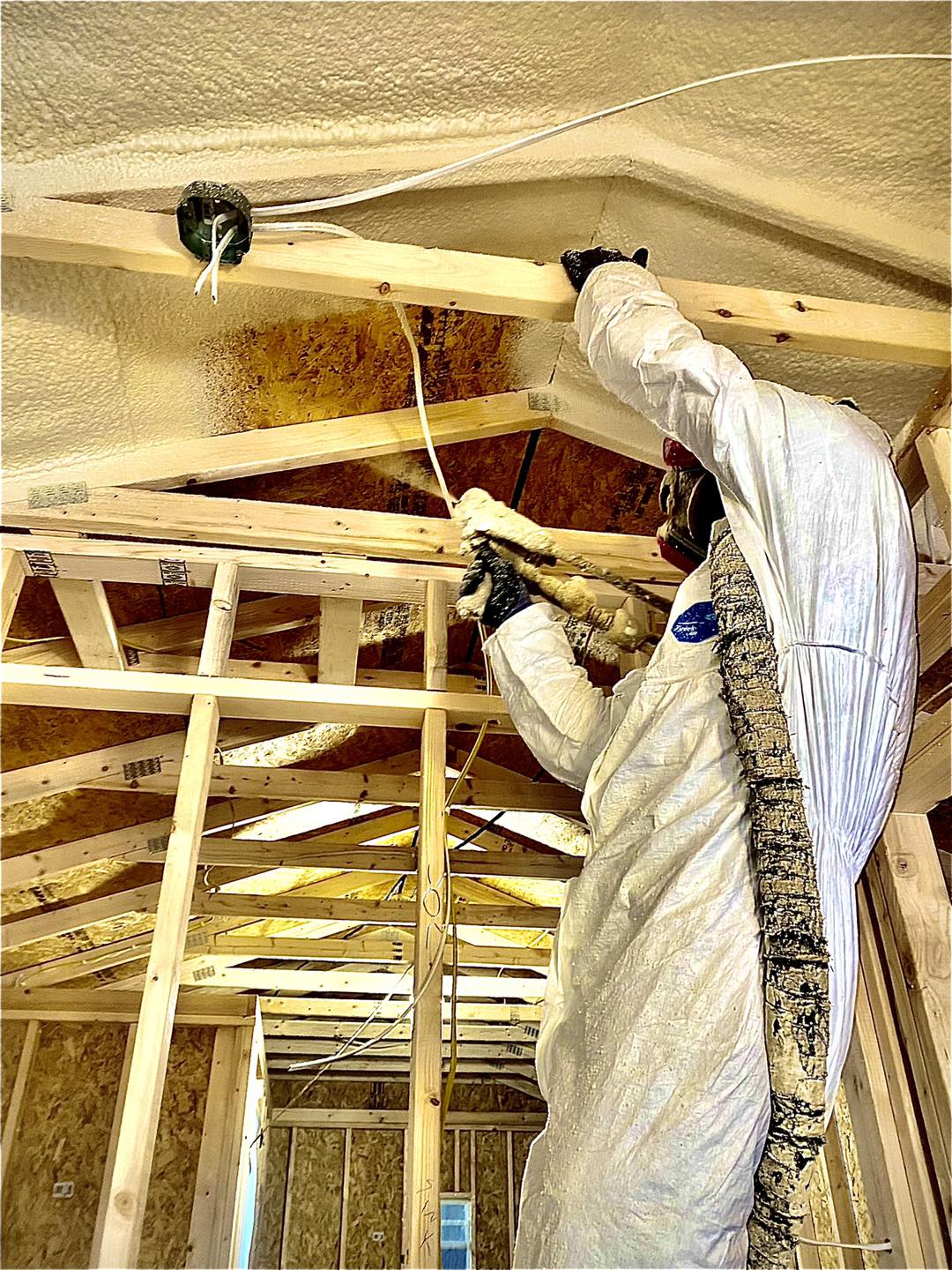 Adult Male standing on a ladder installing Spray Foam Insulation